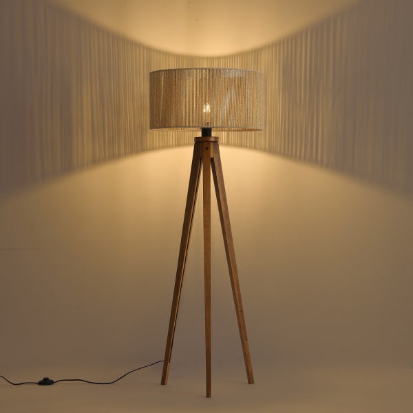 Dreibein-Stehleuchte aus Holz mit rundem Schirm aus feinem Seil, eingeschaltet mit Lichteffekt an der Wand.