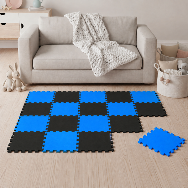 Wohnzimmer mit zusammengesetzten Puzzlematten in Schachbrettmuster auf Holzboden vor einem Sofa mit Decke.