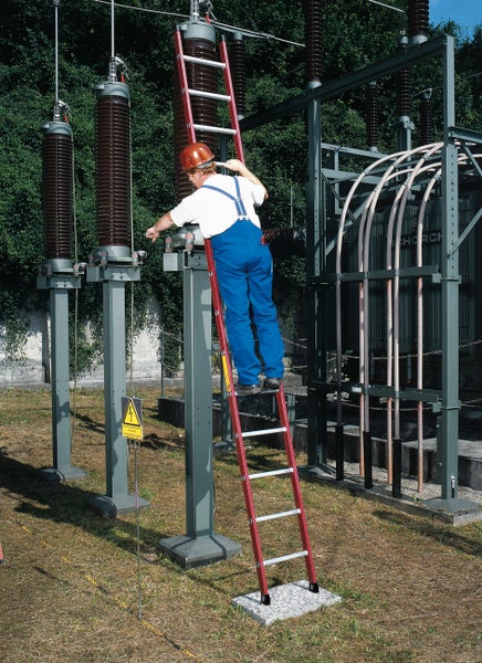 Mann auf einer Leiter in einem Umspannwerk, in der Nähe von Hochspannungstechnik