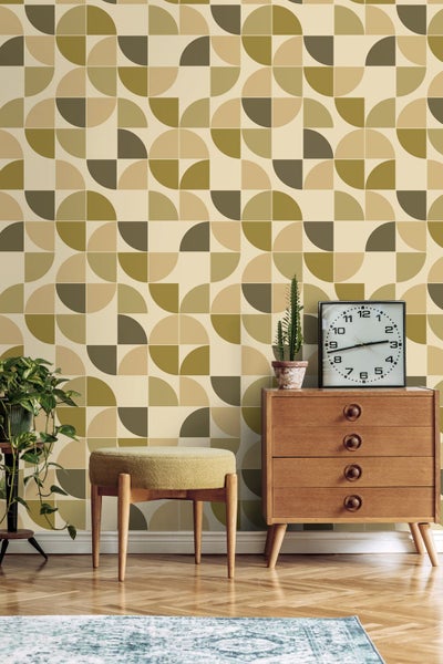 Tapete mit geometrischem Retromuster in Erdtönen kombiniert mit einer Holzkommode, einem runden Hocker und einer Zimmerpflanze.