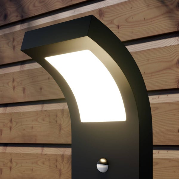 Moderne schwarze Außenleuchte mit Bewegungsmelder an einer Holzwand, integriertes LED-Leuchtmittel leuchtet.