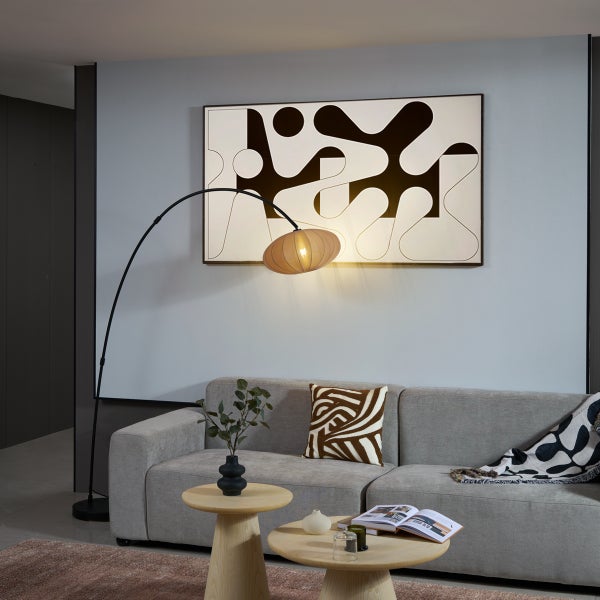 Moderne schwarze Bogenstehlampe mit warmem Schirm über einem grauen Sofa in einem hellen Wohnzimmer mit abstrakter Wandkunst.
