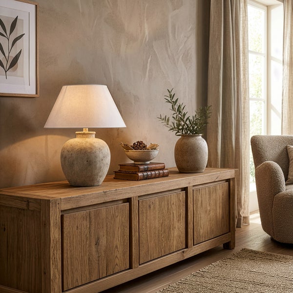 Sideboard aus Massivholz mit Tischleuchte, Vase und Dekoration in einem hellen, rustikalen Wohnzimmer mit strukturierten Wänden.