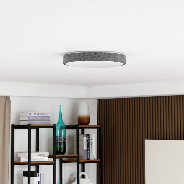 Moderne runde LED-Deckenleuchte mit grauem Stoffrand in hellem Zimmer mit Regal und Holzlamellenwand.