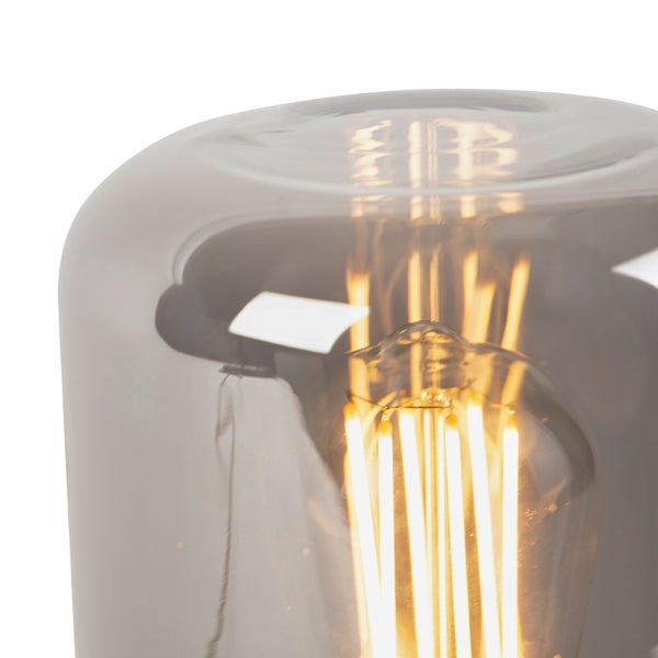 Nahaufnahme eines Leuchtmittels mit sichtbaren Glühfäden in einem rauchfarbenen Glasschirm.