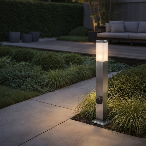 Moderne Wegeleuchte aus Edelstahl mit Steckdose und warmweißem Licht in einem organisierten Garten neben einem Steinweg.