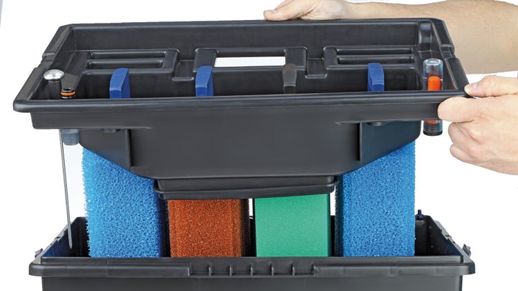 Geöffneter Teichfilter aus Kunststoff mit verschiedenen Filterschäumen, Thermometer und Wasserstandsanzeige, gehalten von Händen.