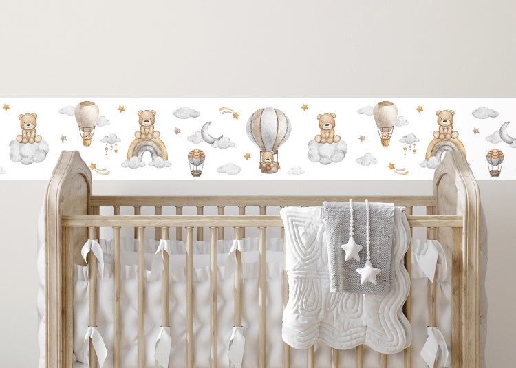 Tapetenbordüre für das Kinderzimmer mit Teddybären, Heißluftballons, Regenbögen und Wolken über einem hölzernen Gitterbett.