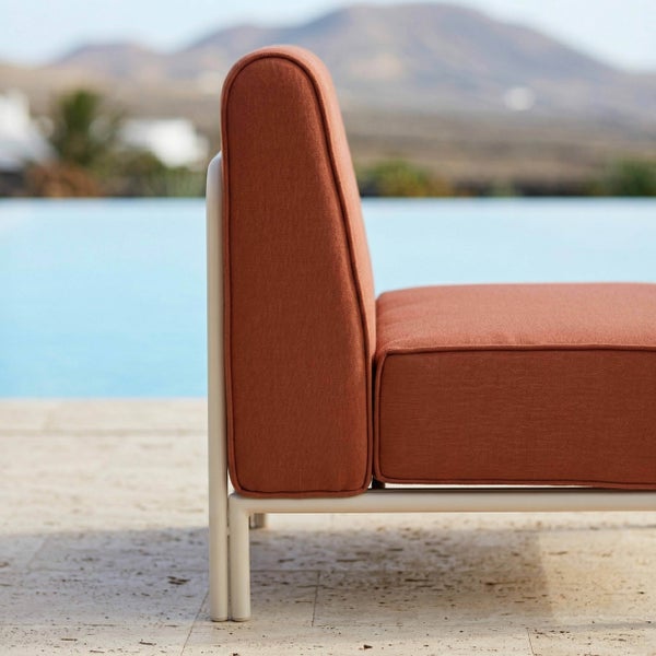 Modernes Outdoor-Loungesofa mit weißem Metallgestell und terracottafarbenen Polstern auf einer Terrasse am Pool.