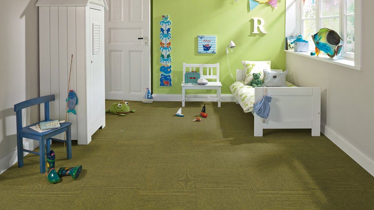 Helles Kinderzimmer mit grünbraunen Teppichfliesen im Schachbrettmuster, weißem Bett, Schrank und blauem Holzstuhl.