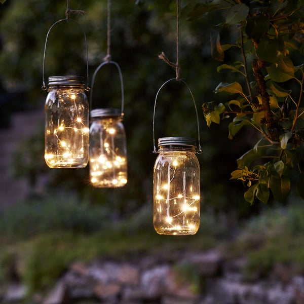 Drei dekorative Einmachglas-Laternen hängen im Garten und sind mit Lichterketten beleuchtet.