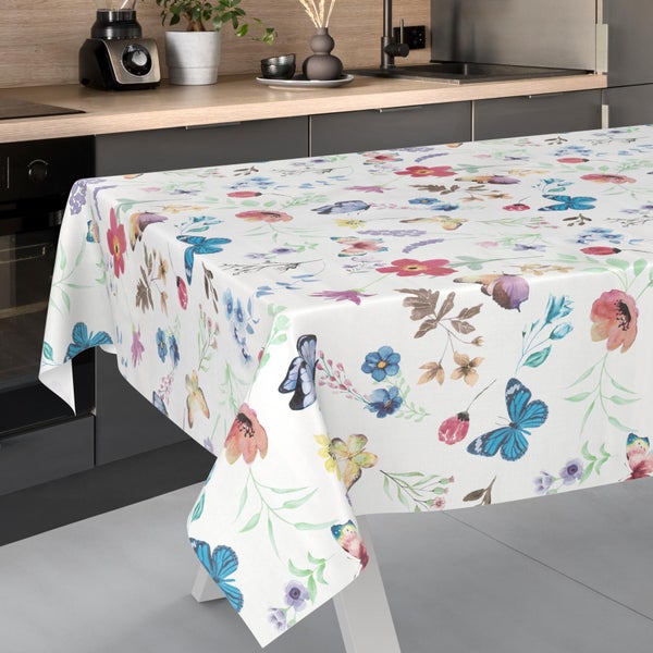 Rechteckige weiße Tischdecke mit buntem Muster aus Blumen und Schmetterlingen auf einem Tisch in einer modernen Küche.