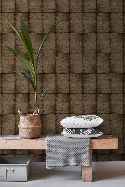 Dekorative Szene mit Pflanze im Korb, Kissen und Textilien auf einer Holzbank vor einer gemusterten Wand