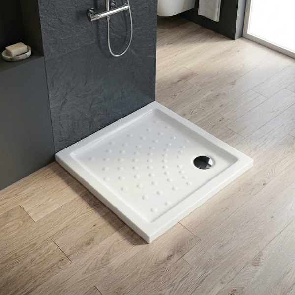 Quadratische Duschwanne mit Noppenstruktur auf hellem Holzboden vor dunkler Wand in einem hellen Badezimmer.