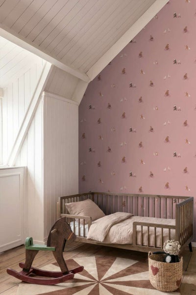 Kinderzimmer mit rosa Tapete mit Tiermotiven, Kinderbett aus Holz, Schaukelpferd und rundem Teppich auf Holzboden.