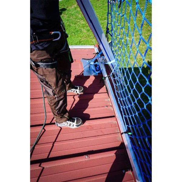 Eine Person mit Sicherheitsausrüstung steht neben einem blauen Sicherheitsnetz auf einem Dach.