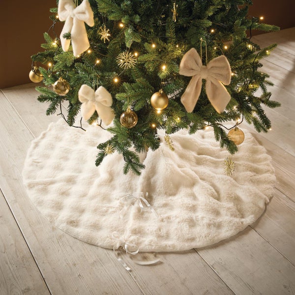 Runder Weihnachtsbaumteppich aus Kunstfell unter einem geschmückten Weihnachtsbaum auf einem Holzboden.