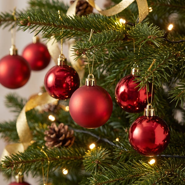 Weihnachtsbaum mit roten Weihnachtskugeln in matt und glänzend sowie goldener Schleife und Lichterkette geschmückt