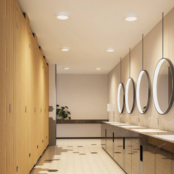 Heller, moderner öffentlicher Sanitärraum mit Holztrennwänden, Steinwaschtisch, beleuchteten Rundspiegeln und LED Einbaustrahlern.