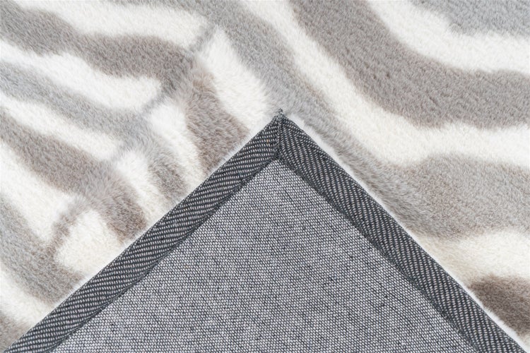 Nahaufnahme eines gemusterten Teppichs mit weicher Oberfläche, umgeschlagener Ecke, Kettelung und strukturierter Rückseite.