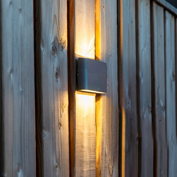 Rechteckige Außenwandleuchte mit Lichtaustritt nach oben und unten, montiert an einem Holzzaun.