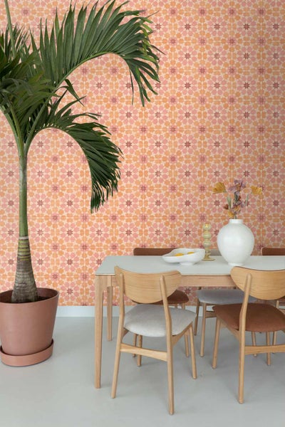Esszimmer mit einer geometrisch gemusterten Tapete in Fliesenoptik, einem Holztisch mit Stühlen und einer großen Zimmerpalme.
