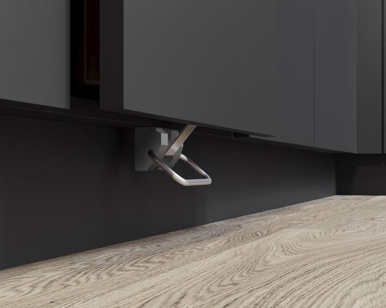 Fußpedal aus Metall für Küchenunterschränke, montiert am dunklen Sockel über hellem Holzboden.