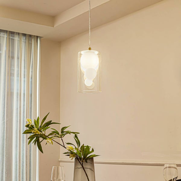 Hängende Pendelleuchte mit einem zylindrischen Schirm aus klarem Glas und weißen dekorativen Kugeln im Inneren in einem hellen Raum.