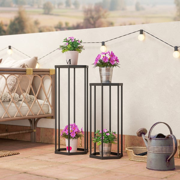 Zwei schwarze Blumenständer aus Metall in verschiedenen Höhen auf einem hellen Balkon, dekoriert mit rosa Blumen in Töpfen.