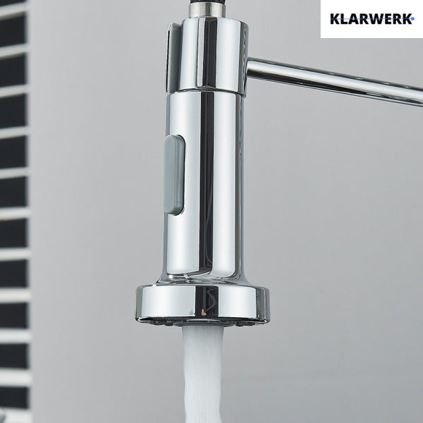 Ausziehbarer Brausekopf einer Küchenarmatur von Klarwerk aus glänzendem Metall mit grauem Bedienknopf und fließendem Wasser. Klarwerk Logo.