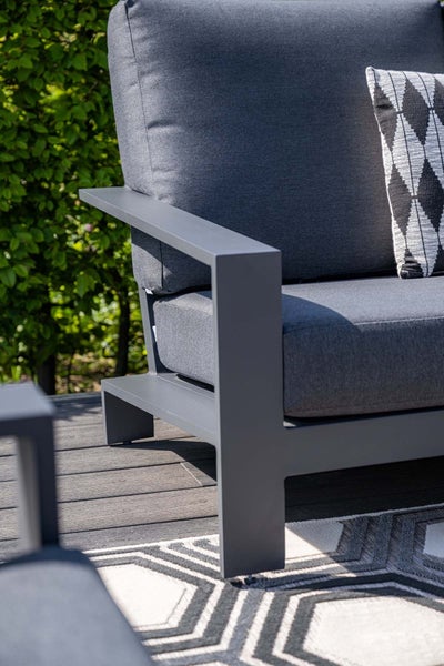 Moderner Garten-Lounge-Sessel mit dunkelgrauem Metallrahmen, grauen Polstern und einem Dekokissen auf einer Holzterrasse.