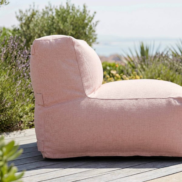 Rosa Outdoor-Sitzsack aus strukturiertem Stoff auf einer Holzterrasse im Garten vor grünen Pflanzen.
