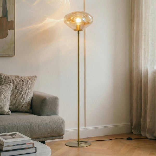 Stehlampe mit gläsernem Lampenschirm und goldenem Gestell neben Couch