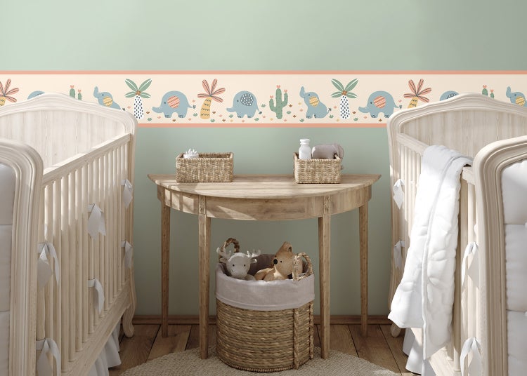 Selbstklebende Tapetenbordüre für Kinderzimmer mit Elefanten, Palmen und Kakteen in einem hellen Zimmer mit zwei Babybetten aus Holz.