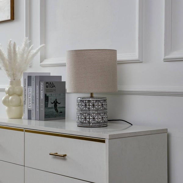 Dekorative Tischleuchte mit geometrischem Muster und Stoffschirm auf einem weißen Nachttisch