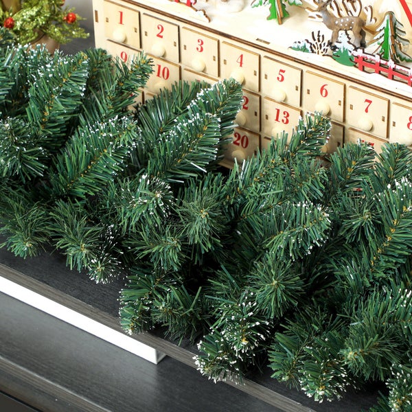 Künstliche Kieferngirlande mit weißen Schneespitzen für die Weihnachtsdekoration vor einem Adventskalender aus Holz.