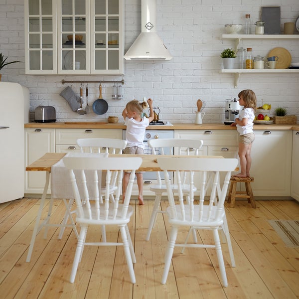 Helle Landhausküche mit Wandhaube über dem Herd und zwei Kindern, die in der Küche spielen.