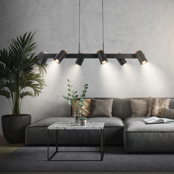 Sechsflammige verstellbare schwarze Pendelleuchte aus Metall mit Holzelementen in einem modern eingerichteten Wohnzimmer mit Sofa und Marmortisch.
