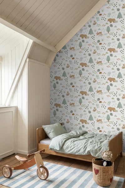 Kindertapete mit Waldtieren wie Bären und Rehen an einer Dachschräge in einem hellen Kinderzimmer mit Holzbett und Spielzeug.