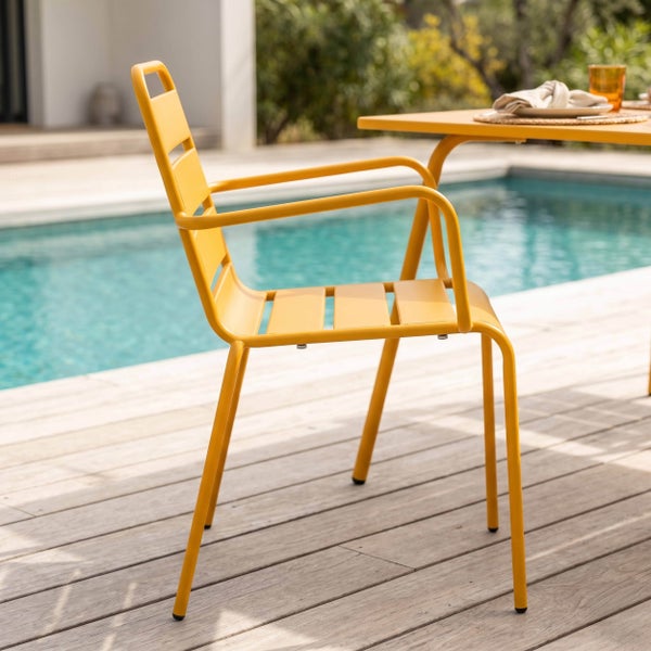 Gelber Gartenstuhl aus Metall mit Armlehnen und Sitzfläche in Lattenoptik auf einer Holzterrasse neben einem Swimmingpool.