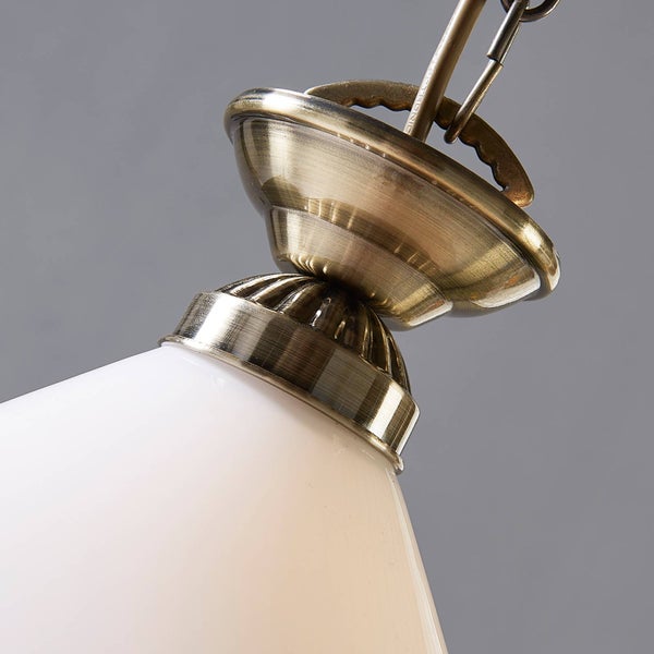 Nahaufnahme einer Pendelleuchte mit einer Metallfassung in Antik-Messing und einem weißem Glasschirm.