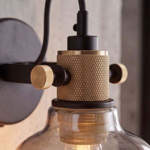 Nahaufnahme einer Wandleuchte im Industriestil mit gerändeltem Metallelement und einem Lampenschirm aus Glas.