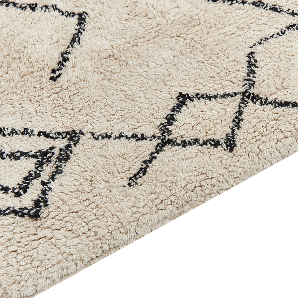 Cremefarbener Teppich mit schwarzem geometrischem Muster auf dunklem Boden im Wohnzimmer mit gelbem Samtsofa und Zimmerpflanzen.