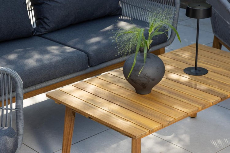 Modernes Garten-Lounge-Set auf einer hellen Terrasse mit einem Sofa aus Seilgeflecht und Textilpolstern sowie einem rechteckigen Holztisch.