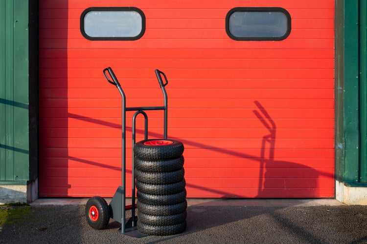 Stapel Reifen auf einer Sackkarre vor einer Garagenwand