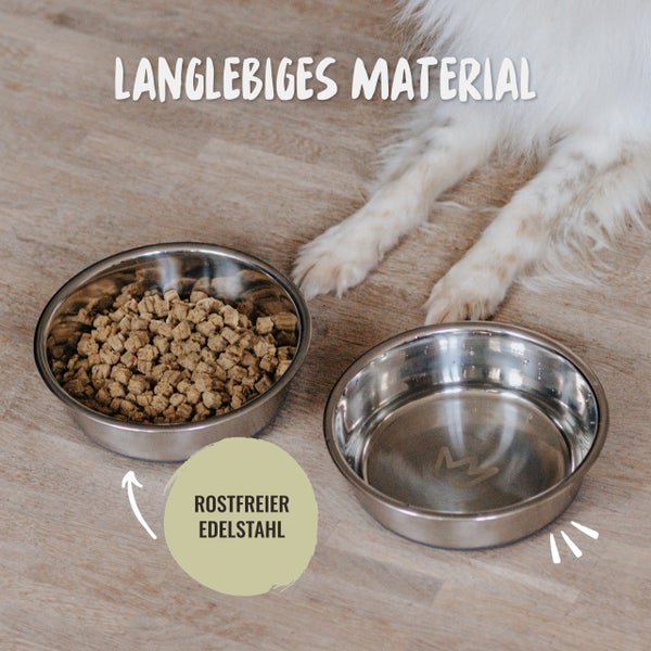 Zwei Edelstahlnäpfe für Hunde, einer gefüllt mit Futter, daneben die Pfoten eines Hundes.