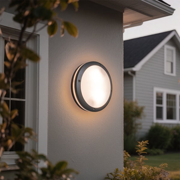 Beleuchtete runde Außenwandleuchte mit dunklem Rahmen an einer Hausfassade.