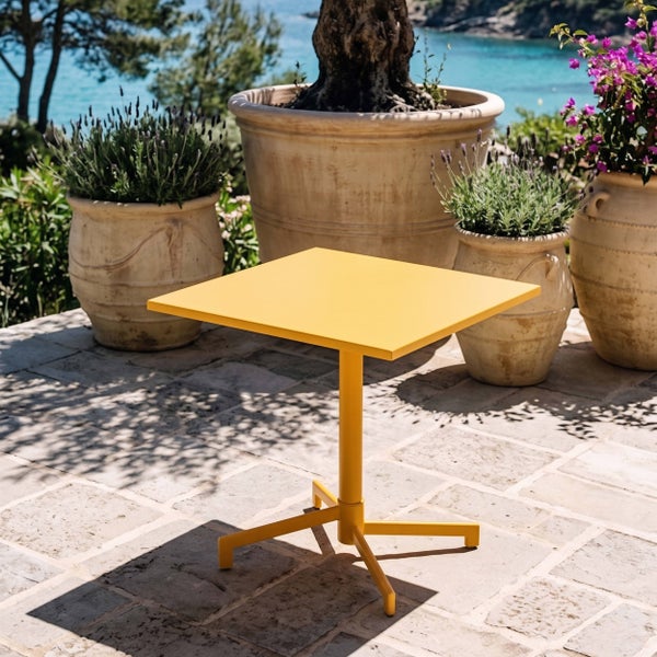 Quadratischer Metall-Bistrotisch auf einer sonnigen Steinterrasse mit Pflanzgefäßen aus Terrakotta und Meerblick.