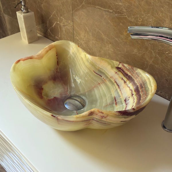 Organisch geformtes Aufsatzwaschbecken aus Onyx Naturstein auf einer Waschtischplatte mit verchromter Armatur.