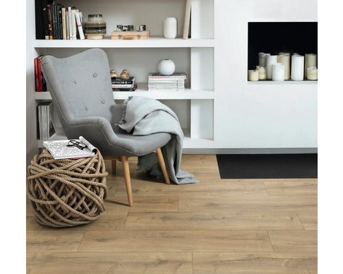 Heller Wohnraum mit modernem Bodenbelag in Holzoptik, grauem Polstersessel und weißem Regalsystem.
